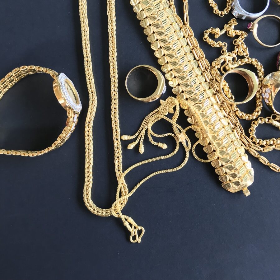 Pile of golden necklace, bracelet and rings on black background